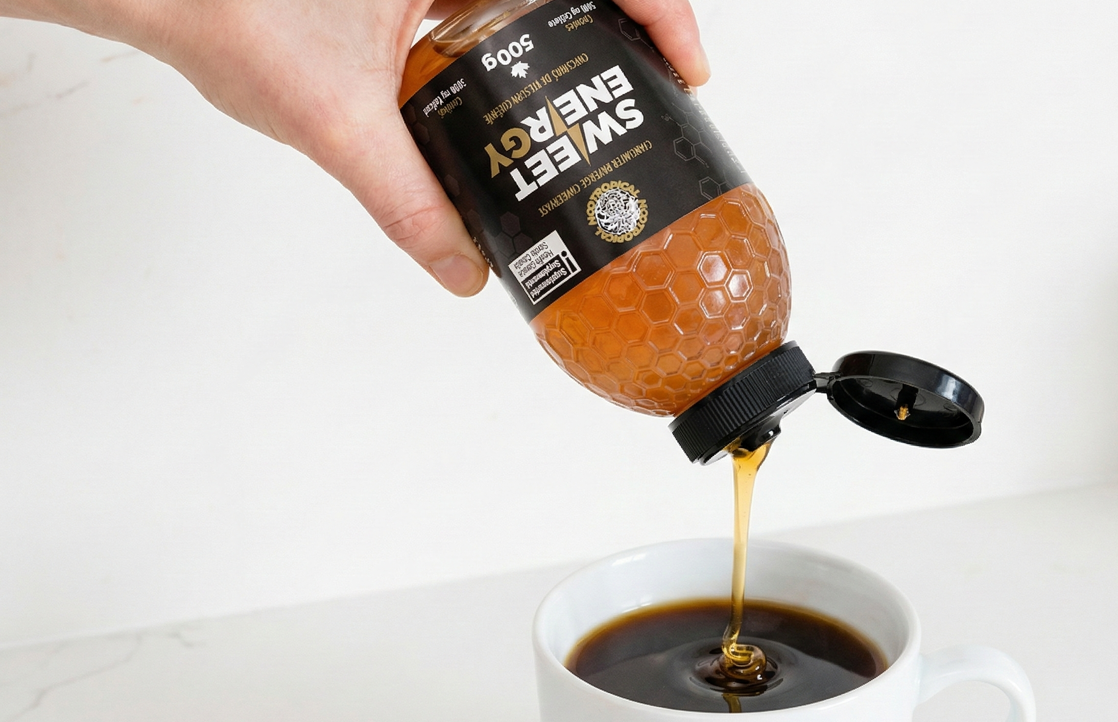 Hand pouring sweetener from a bottle into a cup of coffee on a white background. Nootropical SWEETENERGY